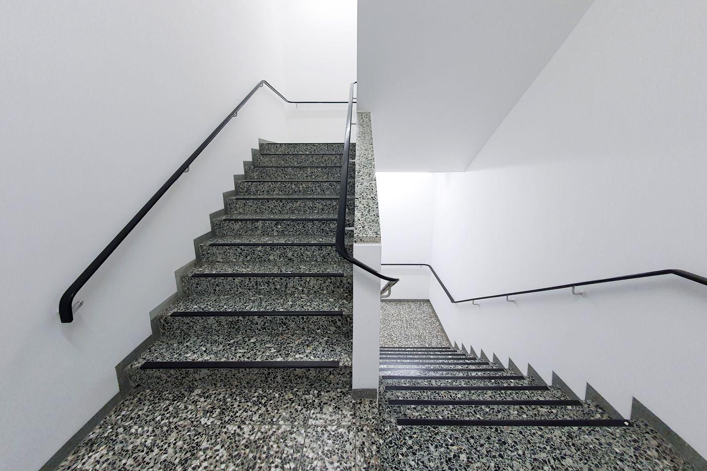 Sauberes Treppenhaus mit hellen Wänden und dunklen Handläufen